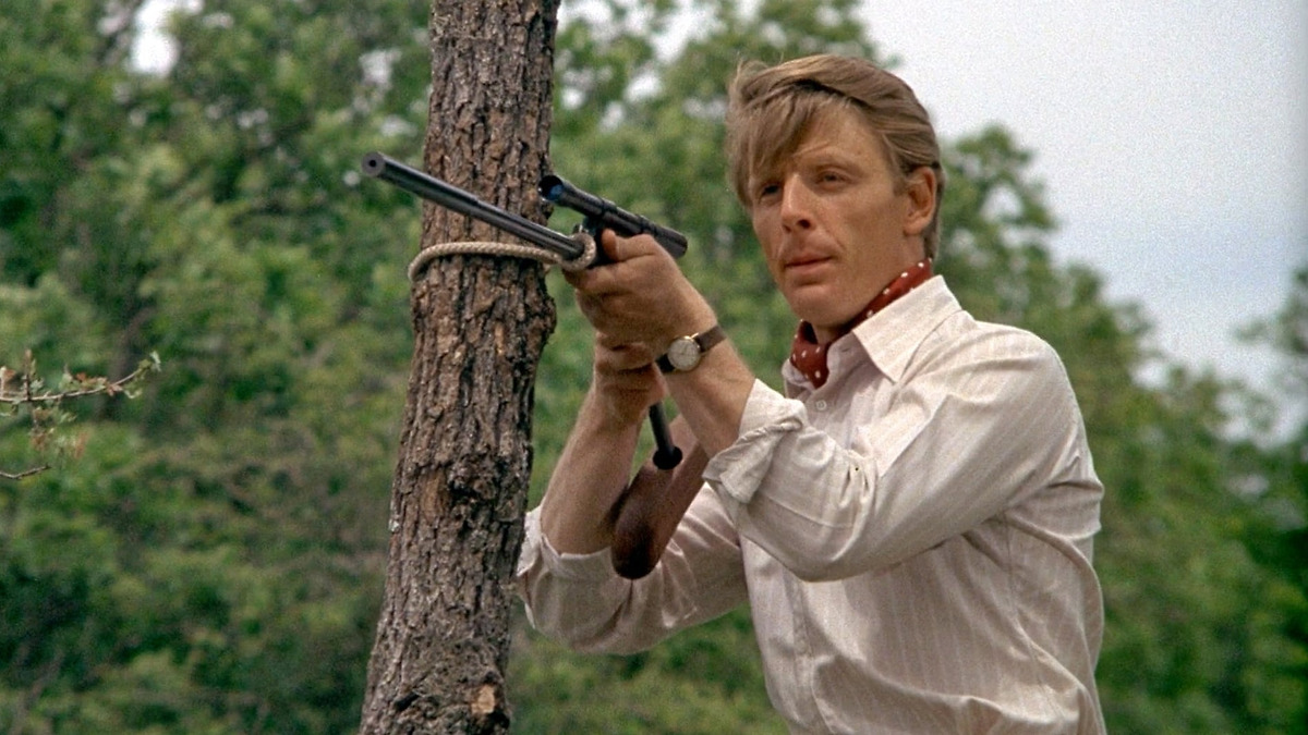 still from The Day of the Jackal (1973) - a sophisticated looking chap aims a strange looking custom made rifle next to a tree
